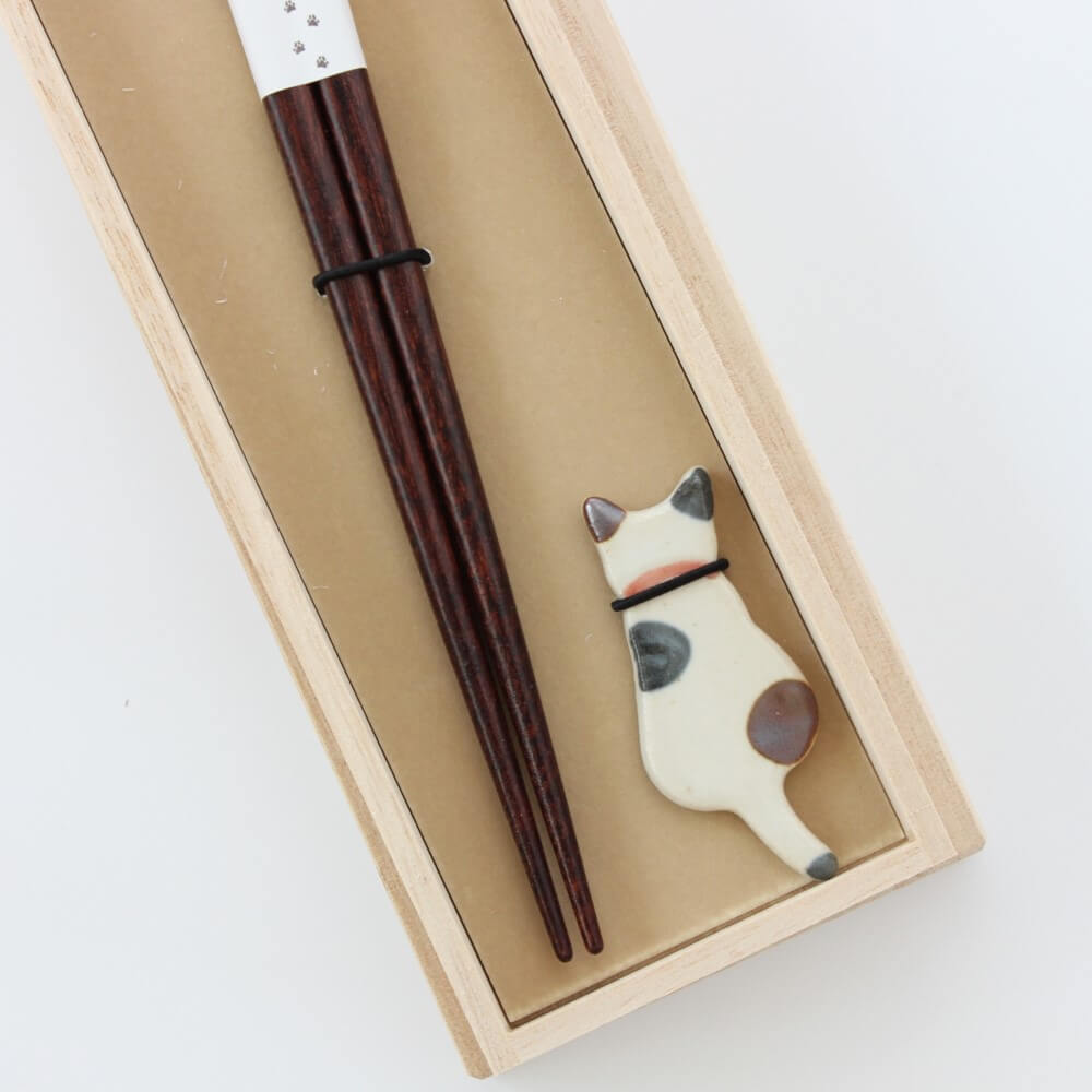 close up calico cat chopsticks rest in box